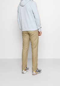 Svetle modrá mikina s kapucí, hnědé slim-fit kalhoty a šedé tenisky se žlutými akcenty. Hladké textury a jednoduchý design.