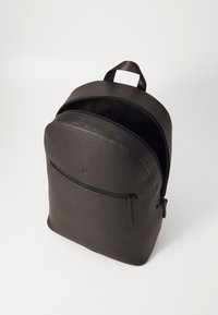 Černý kožený batoh zaobleného tvaru, s přední kapsou na zip a horním držadlem. Hladký povrch a minimalistický design.