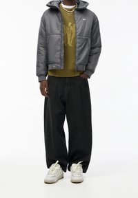 Veste grise rembourrée avec capuche, pull en maille vert olive, jean noir ample et baskets blanches. Textures remarquables et superposition présentes.