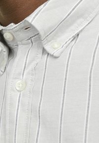 Koszula zapinana na guziki w białym materiale z cienkimi szarymi paskami, z klasycznym kołnierzykiem i perłowymi guziczkami, prezentująca teksturowany splot.