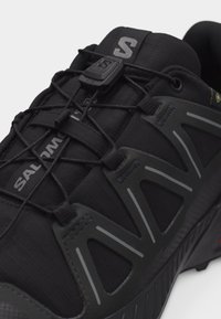 Μαύρο αθλητικό παπούτσι Salomon με κορδόνια γρήγορης έλξης, επάνω μέρος από διαπνέον πλέγμα και τριγωνικά πλευρικά καλύμματα με αντανακλαστικές λεπτομέρειες.