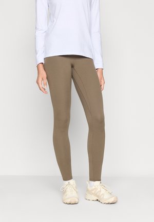 Leggings marron au design ajusté et aux détails de couture, associés à une chemise à manches longues légère et des chaussures de sport beiges.