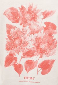 Balta T-krekls ar korallveida ziedu zīmējumu, kurā redzami saulespuķes un lapas, ar detaļām izstrādātām kontūrām un maigu tekstūru. Apakšā ir drukāts zīmola nosaukums "MUSTANG".