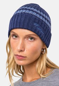 Beanie navale lavorato a maglia con texture a coste, caratterizzato da strisce azzurro chiaro e ricami sottili. Materiale morbido e caldo adatto per il clima freddo.