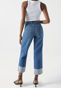 Jeans azul de cintura alta con corte recto, que presentan un dobladillo acampanado en un tono más claro, bolsillos traseros y detalles de costura.