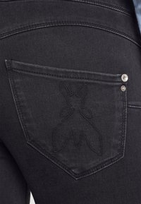 Jeans de mezclilla negra con un diseño de bolsillo cosido con un patrón floral, remaches metálicos y una textura suave.