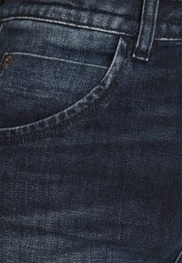 Jeans in denim blu scuro con una texture liscia, caratterizzati da una tasca curvata, sbiaditure sottili e cuciture in contrasto. Design classico a cinque tasche.