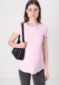 Rožinė banguota t-shirt su trumpomis rankovėmis ir banguota apačia, derinama su juodu rankiniu krepšiu. Fonas – paprastas šviesus.