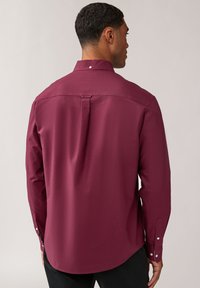 Camicia bordeaux a maniche lunghe con colletto button-down, piega centrale sul retro e dettagli in bianco sui polsini; tessuto dalle linee morbide.