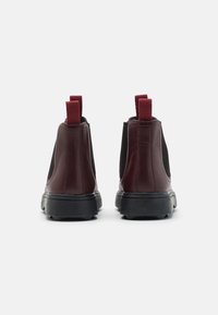 Burgundy läder ankelskor med elastiska sidopaneler, en texturerad svart gummisula och två dragflikar bak för enkel påtagning.