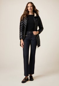 Zwarte gewatteerde jas met beige kraag, gecombineerd met donkerdenim hoge taille broek met onderscheidende stiksel- en hardwaredetails.