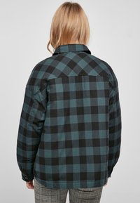 Camisa de franela a cuadros en negro y azul verdoso con un ajuste relajado, mangas largas y collar. Presenta un dobladillo recto y puños abotonados.