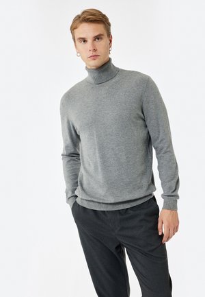 Grauer Rollkragenpullover aus weichem Stoff, mit langen Ärmeln und taillierter Passform. Kombiniert mit dunklen Hosen für einen minimalistischen Look.