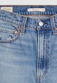 Jean en denim bleu avec un délavage clair, des ferrures en cuivre et un design standard à cinq poches. L'étiquette indique "Ribcage Bell" et taille "27."