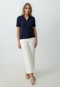 Granatowa koszulka polo z krótkim rękawem i dekoltem w serek, zestawiona z białymi szerokimi spodniami i beżowymi mokasynami. Gładki materiał i dopasowany krój.