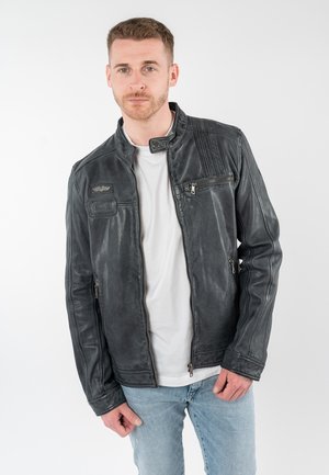 Zwarte leren jas met een getailleerd ontwerp, voorzien van een hoge kraag, ritsen en patches. Soepele textuur met een subtiele glans.