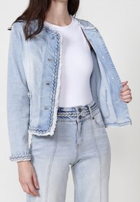 Light blue denim jacket with frayed edges, braided accents, and button closures. Paired with matching high-waisted jeans, also in light blue.