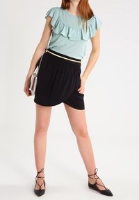 Světle modrý volánkový top v kombinaci s černou sukní s zakřiveným lemem. Modelka má na nohou černé baleríny s kotníkovými pásky. Stříbrná kabelka přes rameno.