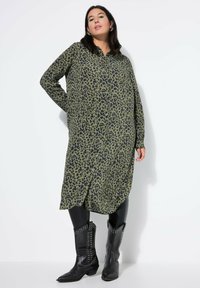 Vestido de botón con estampado de leopardo en verde oliva, con mangas largas, corte holgado y aberturas laterales, combinado con botas de cowboy negras con tachuelas.
