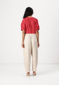 Red patterned blouse with puff sleeves paired with loose, beige, linen trousers. Trousers feature elastic waist and back pockets.