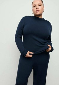 Set de lounge tricotat albastru marin, format dintr-un top cu mâneci lungi și gât rotund și pantaloni mulați asortați, prezentat pe un fundal deschis.