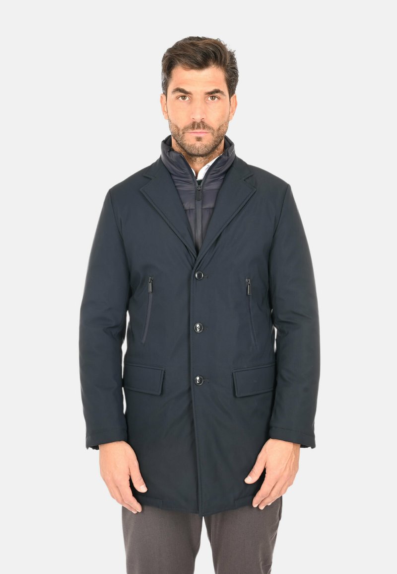 Cappotto blu navy con chiusura frontale a bottoni, ampi revers, due tasche con cerniera e una fodera interna trapuntata, realizzato in tessuto liscio e strutturato.