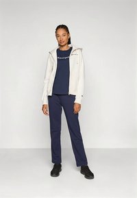 Sweat à capuche zippé de couleur claire, t-shirt bleu marine avec logo, pantalon bleu marine et chaussures noires ; tenue décontractée avec des couleurs contrastantes et une coupe ample.