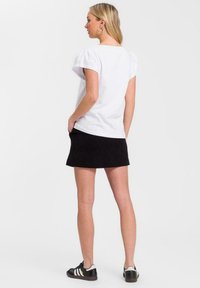 Biała bawełniana koszulka z krótkimi bufkami, zestawiona z czarną spódnicą. Modelka nosi czarne sneakersy w białe paski oraz srebrne kolczyki w kształcie kół.