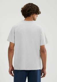 Graues Baumwoll-T-Shirt mit kurzen Ärmeln und Rundhalsausschnitt, von hinten gezeigt. Weiche Textur und lockere Passform sichtbar.