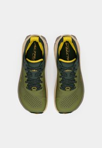 Chaussures de trail running vertes avec un dessus texturé, des accents jaunes, un col rembourré et des lacets. La semelle est de couleur beige avec des détails de traction.