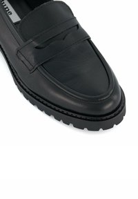 Black leather loafer with a smooth finish, featuring a decorative strap across the upper and a thick, textured rubber sole.