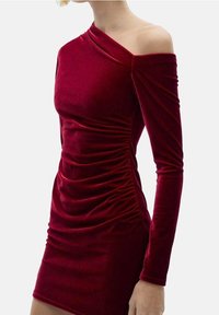 Robe en velours rouge avec une manche dénudée, des fronces sur le côté et une coupe ajustée épousant la silhouette.