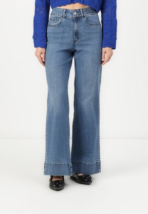 Jeans a vita alta, a gamba larga, di colore blu chiaro con cuciture sottili, cinque tasche, chiusura con bottone e borchie argentate lungo le cuciture laterali.