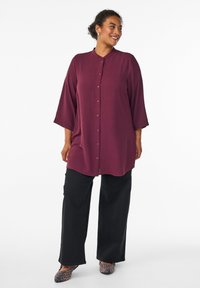 Burgundy button-up shirt with a high collar, three-quarter sleeves, and a relaxed fit, paired with black wide-leg pants and patterned flats.