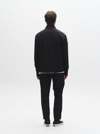 Melnā vieglā jaka ar apkakli, saskaņota ar melnām biksēm un sporta apaviem. Vienkāršs dizains, viendabīga krāsa un brīvs piegriezums.