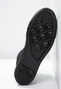 Svart gummisula för sneakers med texturerade geometriska mönster, som har präglad branding och en hållbar slitbanedesign för grepp.