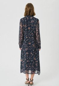 Rochie florală marină cu mâneci lungi din material transparent, cu guler înalt și o siluetă fluidă. Model cu flori mici roz și albe pe toată suprafața.