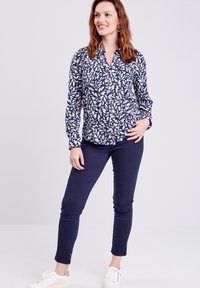Camicia blu navy con motivo a foglia bianca, maniche lunghe e colletto. Indossata con pantaloni slim blu navy e sneakers chiare.