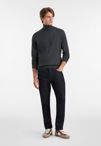 Dunkelgrauer, strukturierter Rollkragenpullover, kombiniert mit dunklen Jeans und beigen Sneakers mit braunen Akzenten. Klassisches und elegantes Design.