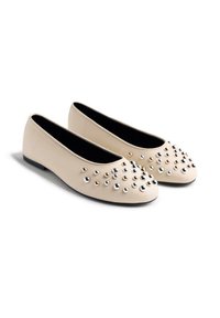 Bailarinas beige con una textura suave, adornadas con tachuelas metálicas en plata y oro en la zona de los dedos; interior negro y suela plana.
