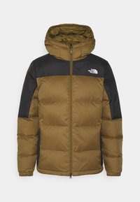 Puffjacka med en gyllenbrun kropp, svarta accenter på ärmar och axlar, hel dragkedja och huva.