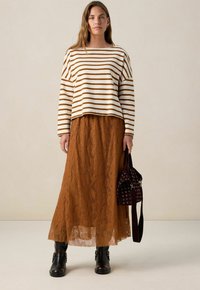 Striped cream and brown sweater, paired with a long, lace, orange-brown skirt; black ankle boots and a textured, dark handbag.