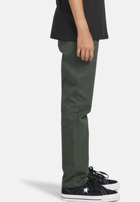 Groene katoenen broek met een rechte pasvorm, voorzien van zijzakken, gedragen met zwarte sneakers met een witte zool en steraccent.
