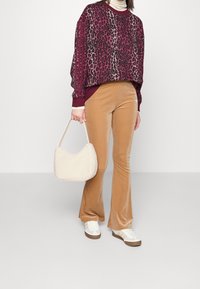 Viininpunainen ja beige leokuosinen collegepaita, yhdistettynä ruskeisiin liehuhousuihin ja valkoisiin lenkkareihin. Mukana pehmeä, vaalea käsilaukku.