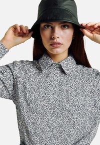 Camicia a bottoni in bianco e nero con colletto, abbinata a un cappello a secchiello verde scuro con un piccolo logo.