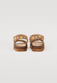 Des sandales marron avec une semelle plate, ornées de broderies florales multicolores sur les lanières. Design à enfiler avec des fermetures ajustables.