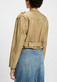 Veste en cuir cropped beige clair avec épaulettes. Caractérisée par une taille ceinturée et une finition texturée. Associée à un denim bleu texturé.
