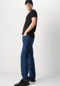 Must have lühikeste varrukatega must T-särk, sinised sirged teksapüksid ja mustad lipsuga kingad. Teksad on sileda tekstuuriga ja klassikalise viie taskuga disainiga.