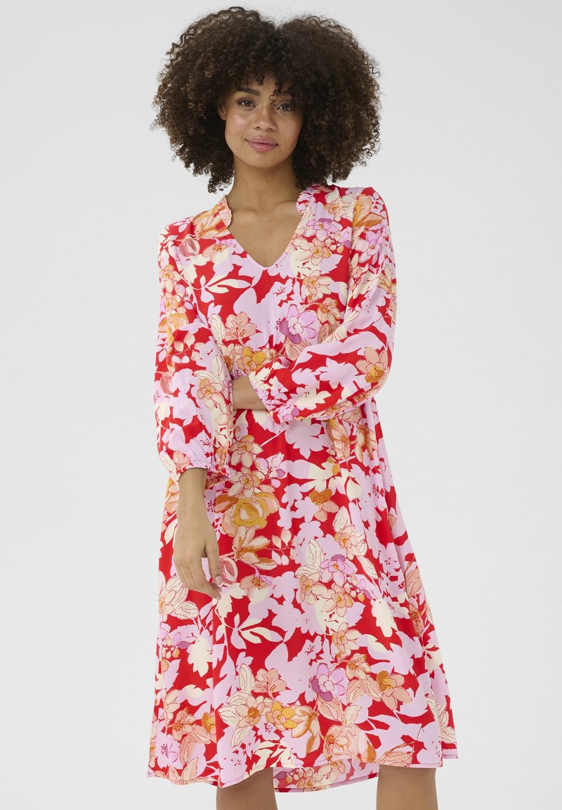 Lillelille kleit V-kaelusega, mis on kaunistatud suurte roosa ja punase lilledega roosa tausta peal. Pikad varrukad kogutud mansettidega. Sile kangas.