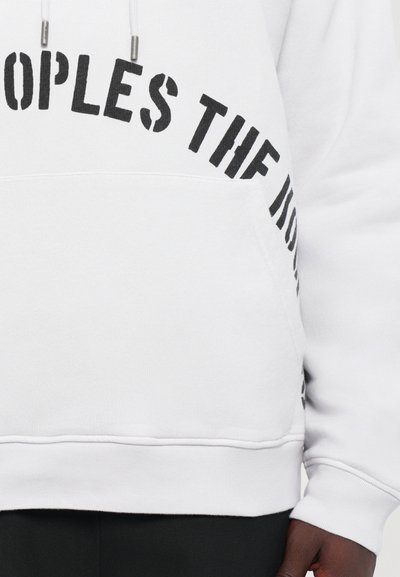 Weißer Hoodie mit schwarzem Blocktext auf der Brust und einer vorderen Tasche, getragen von einer Person mit dunkler Hautfarbe und schwarzen Hosen.